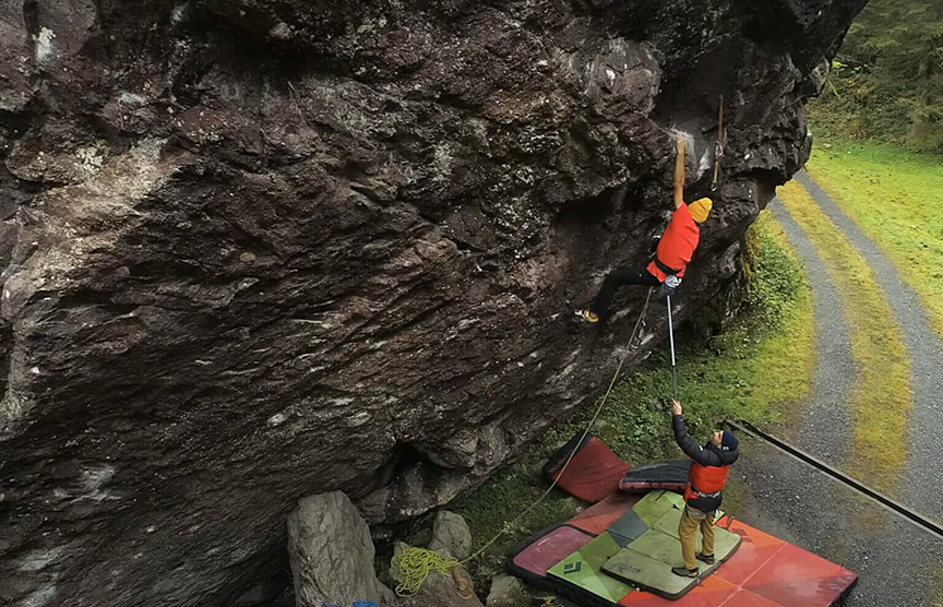 climber on a big steep boulder receiving a rope and gear on the end of a pole from the ground